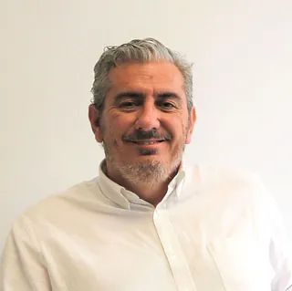 Un hombre con barba lleva una camisa blanca y sonríe.