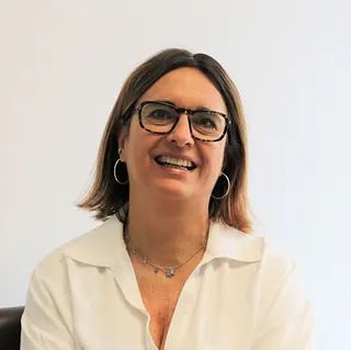 Una mujer que lleva gafas y una camisa blanca está sonriendo.