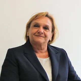 Una mujer con una chaqueta azul y una camisa blanca sonríe a la cámara.