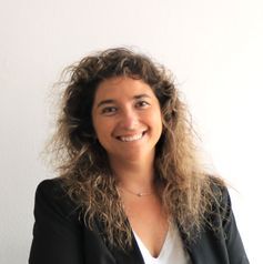 Una mujer con cabello rizado lleva una chaqueta negra y sonríe.