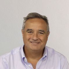 Un hombre con una camisa morada sonríe a la cámara.