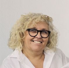 Una mujer que lleva gafas y una camisa blanca está sonriendo.