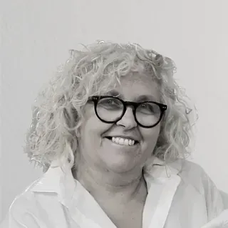 Una mujer que lleva gafas y una camisa blanca sonríe en una foto en blanco y negro.