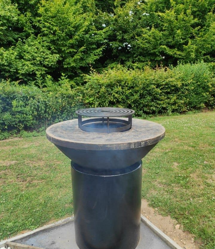 Brasero barbecue rond, installé dans un jardin verdoyant.