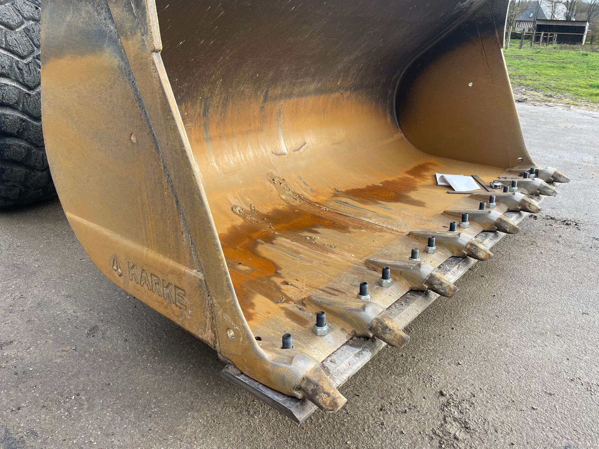Gros plan sur un godet de pelle mécanique jaune à dents, posé sur du gravier.