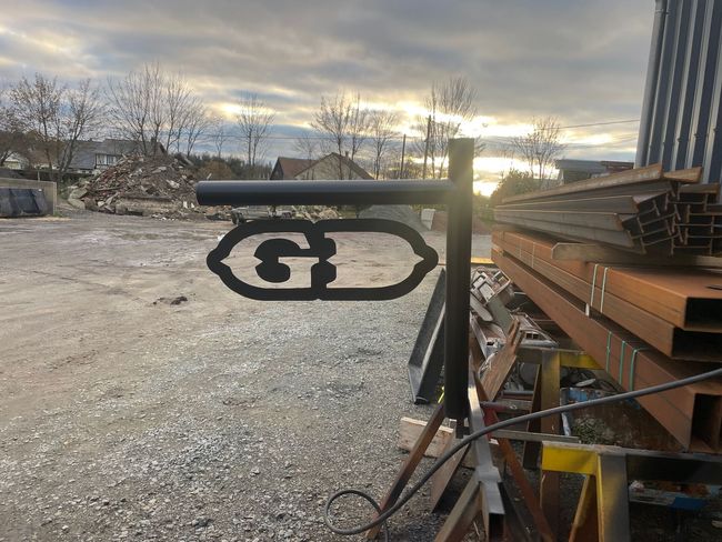 Panneau métallique avec pièce découpée en forme de lettres, dans une cour industrielle avec poutrelles en acier.