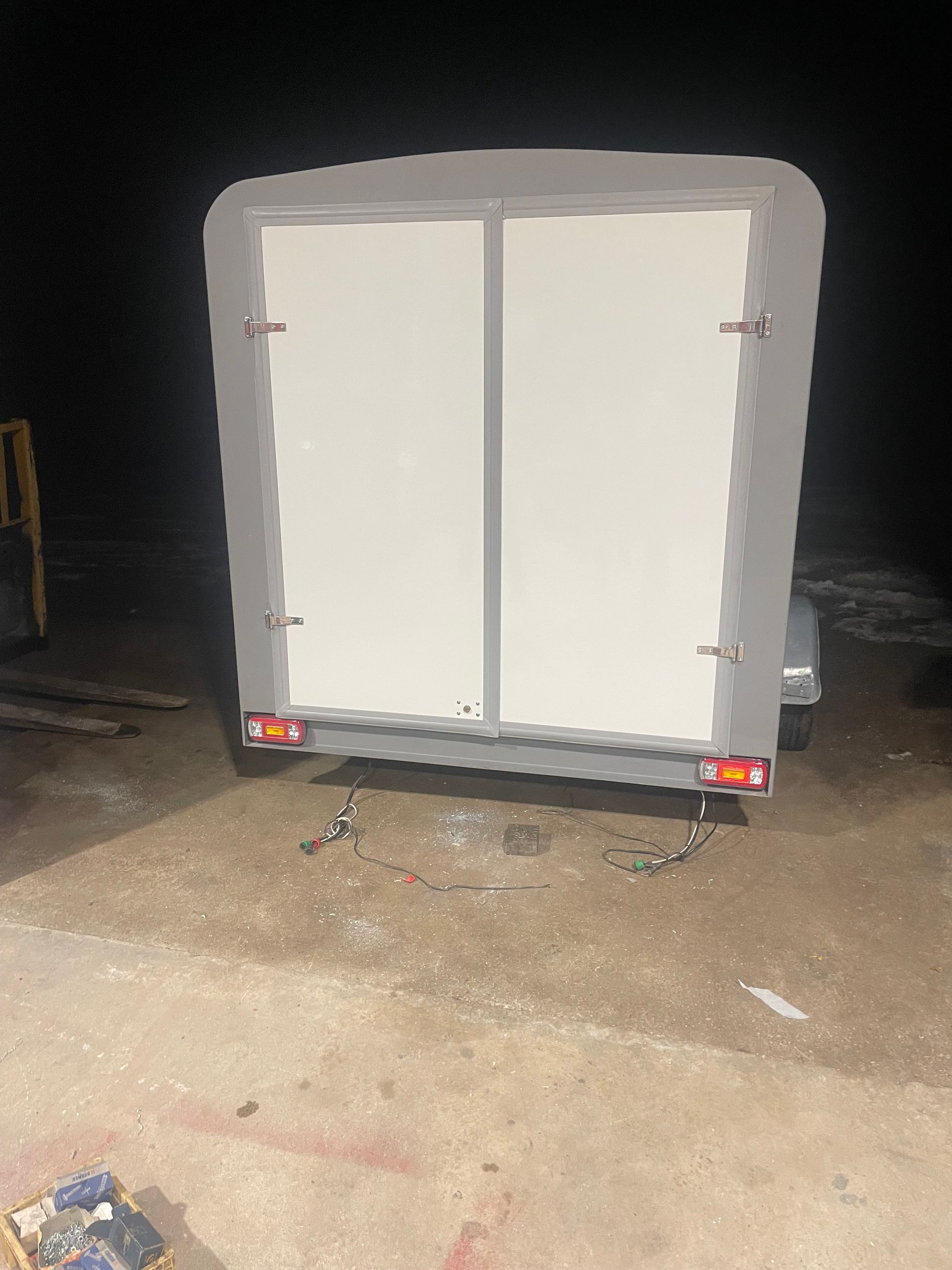 Arrière d’une remorque fermée avec double porte battante blanche et feux arrière allumés dans un atelier.