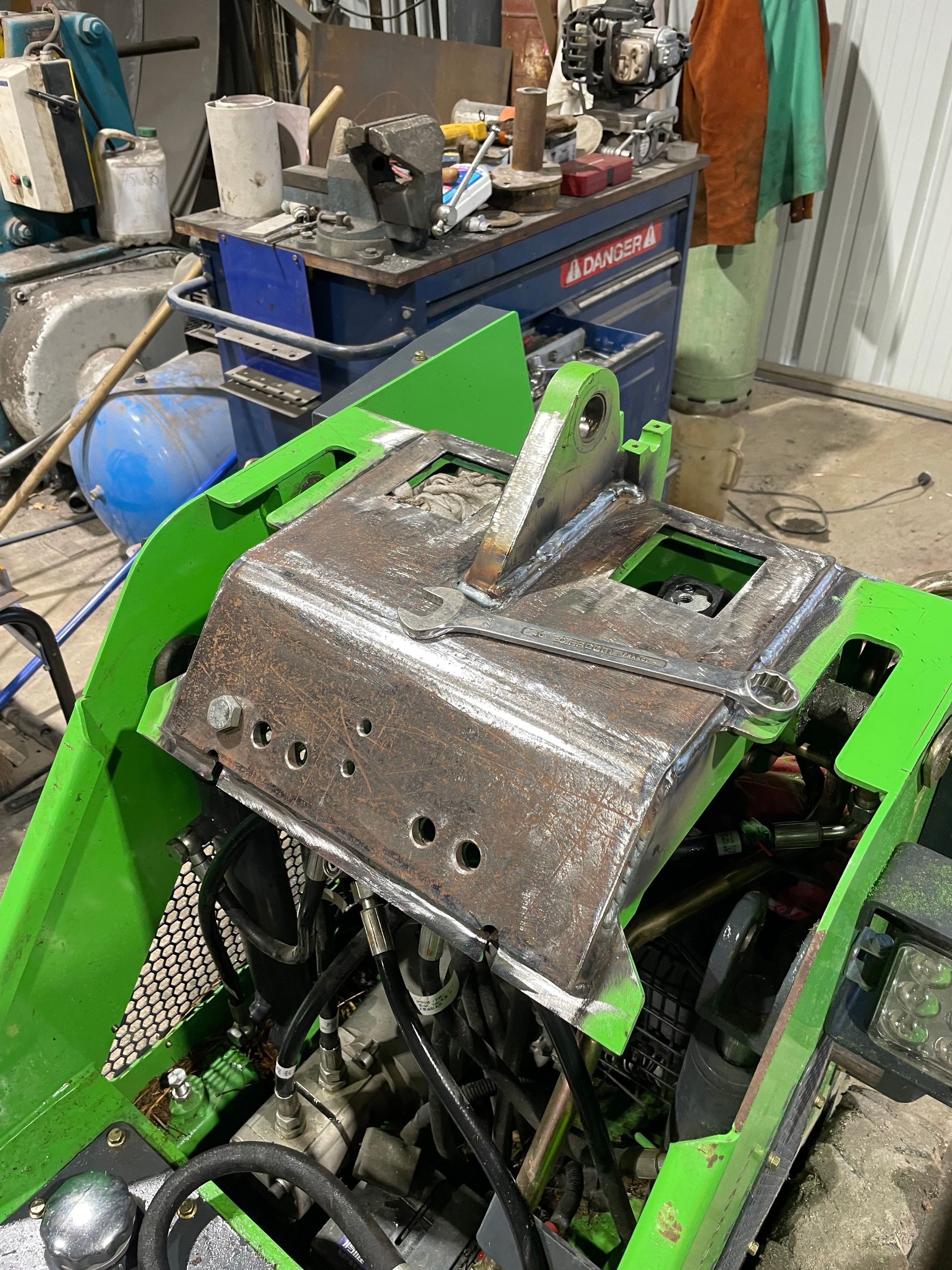 Réparation d'une chargeuse compacte verte dans un atelier de maintenance.