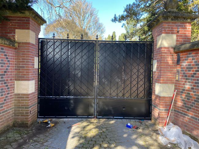 Un double portail en métal noir, encadré par des piliers en briques.