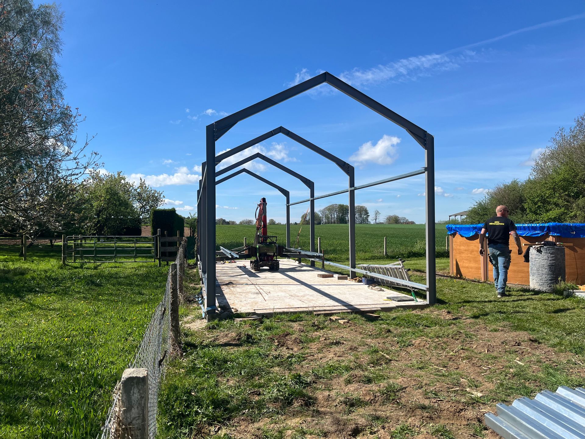 Une structure à ossature métallique dans un jardin, avec un ouvrir une piscine hors-sol sur la droite.