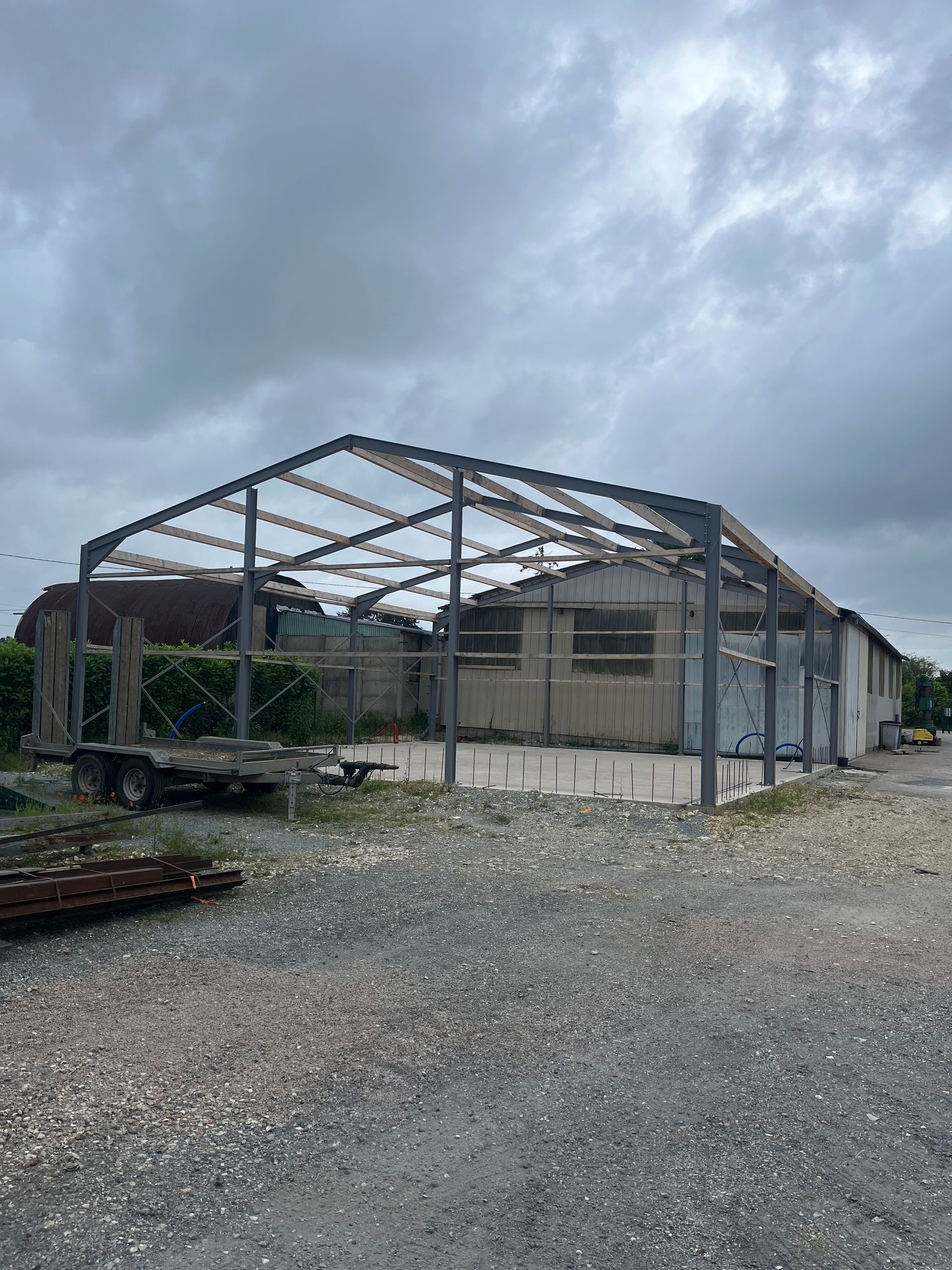 Ossature métallique d'un hangar ou d'un bâtiment industriel en construction, avec charpente en bois et acier.
