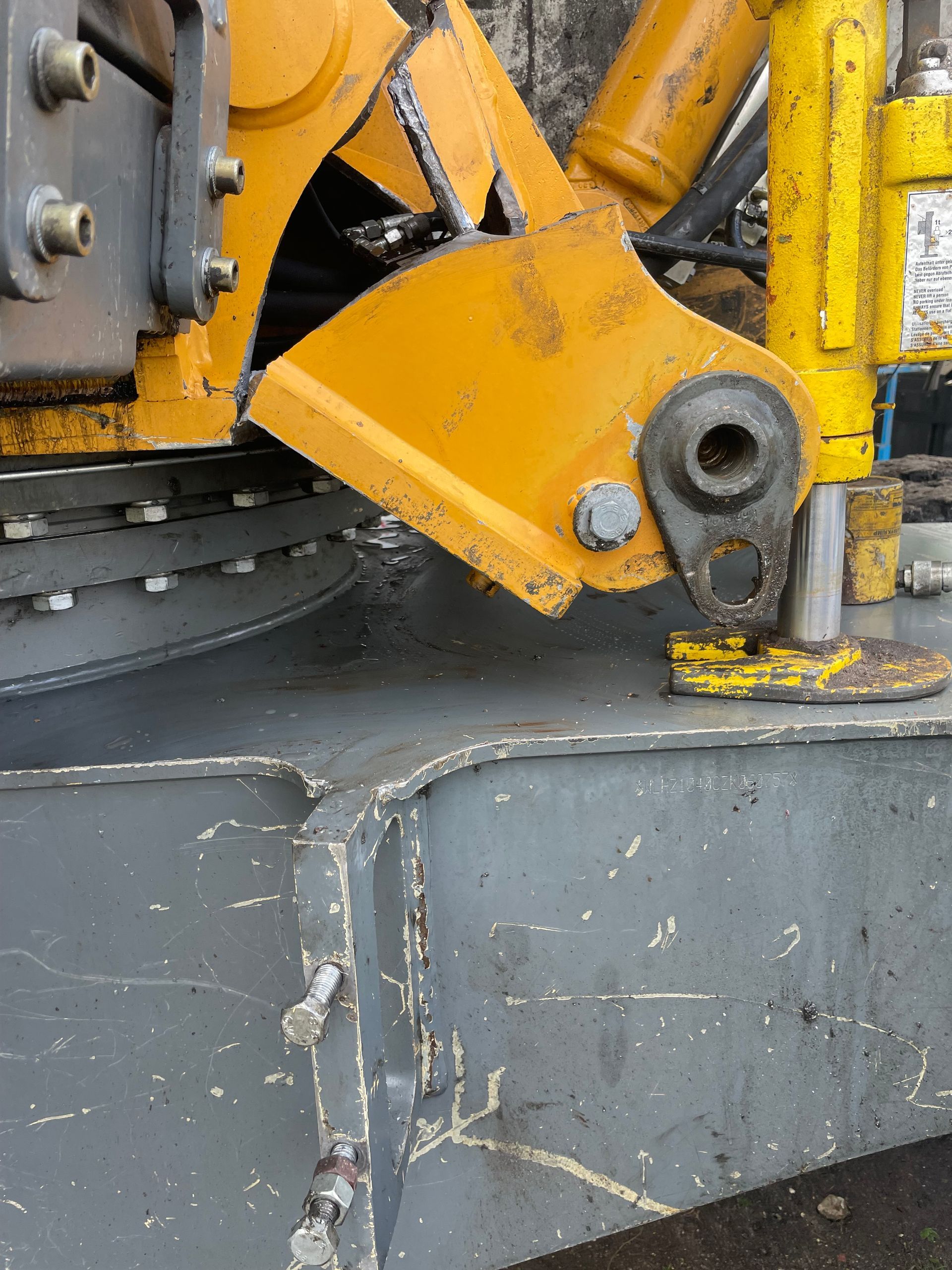 Gros plan sur un bras de machine jaune avec une articulation boulonnée, monté sur une base métallique grise.