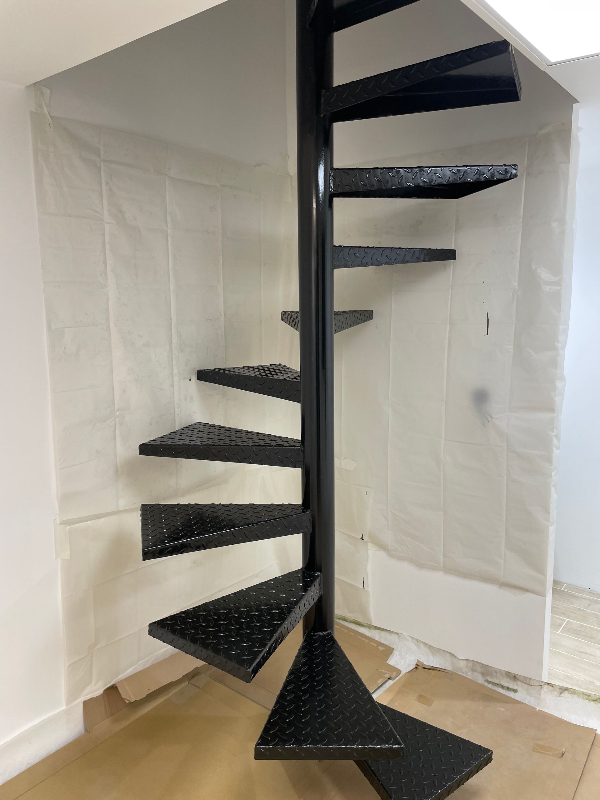 Escalier en colimaçon métallique noir, dans une pièce en construction.
