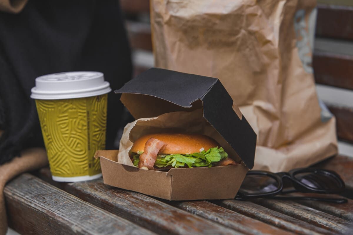 Una hamburguesa y una taza de café están sentadas en un banco de madera.