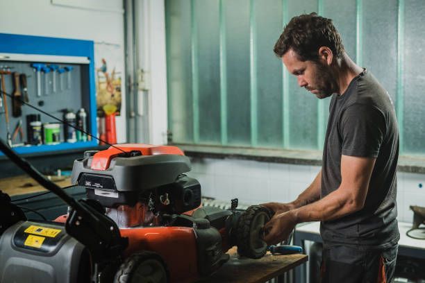 Une personne penchée sur une machine dans une allée d'atelier, vêtue d'une chemise rayée et d'un pantalon foncé
