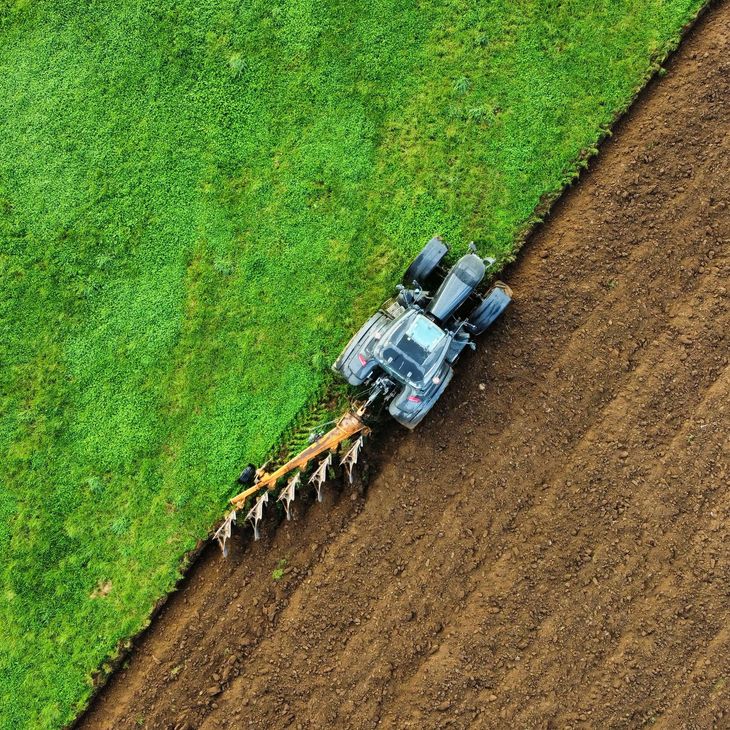 Un tracteur laboure un champ, traçant une bande brune à côté d'une herbe d'un vert éclatant.