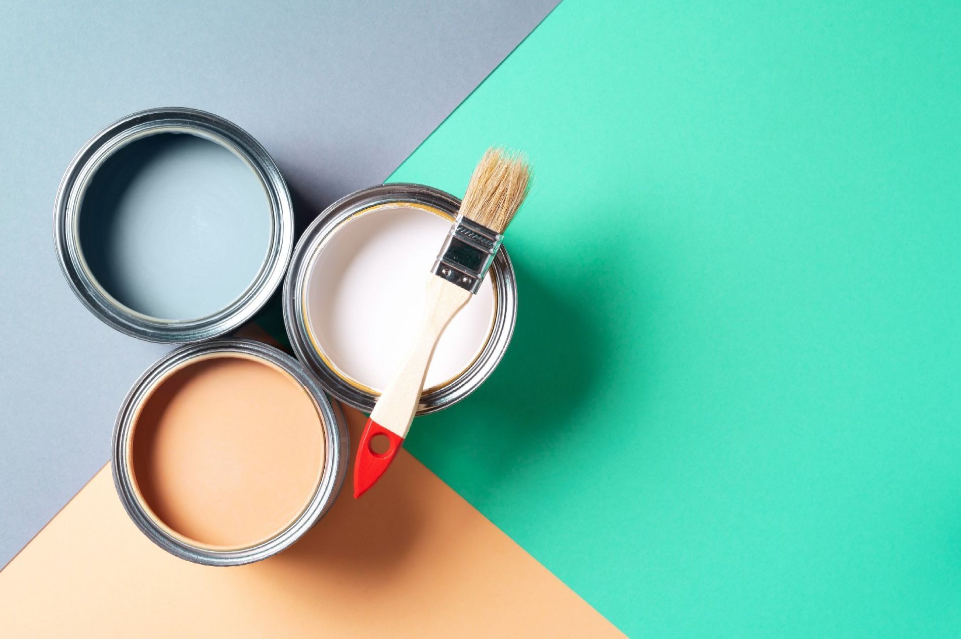 Tres latas de pintura y un pincel sobre un fondo verde y naranja.
