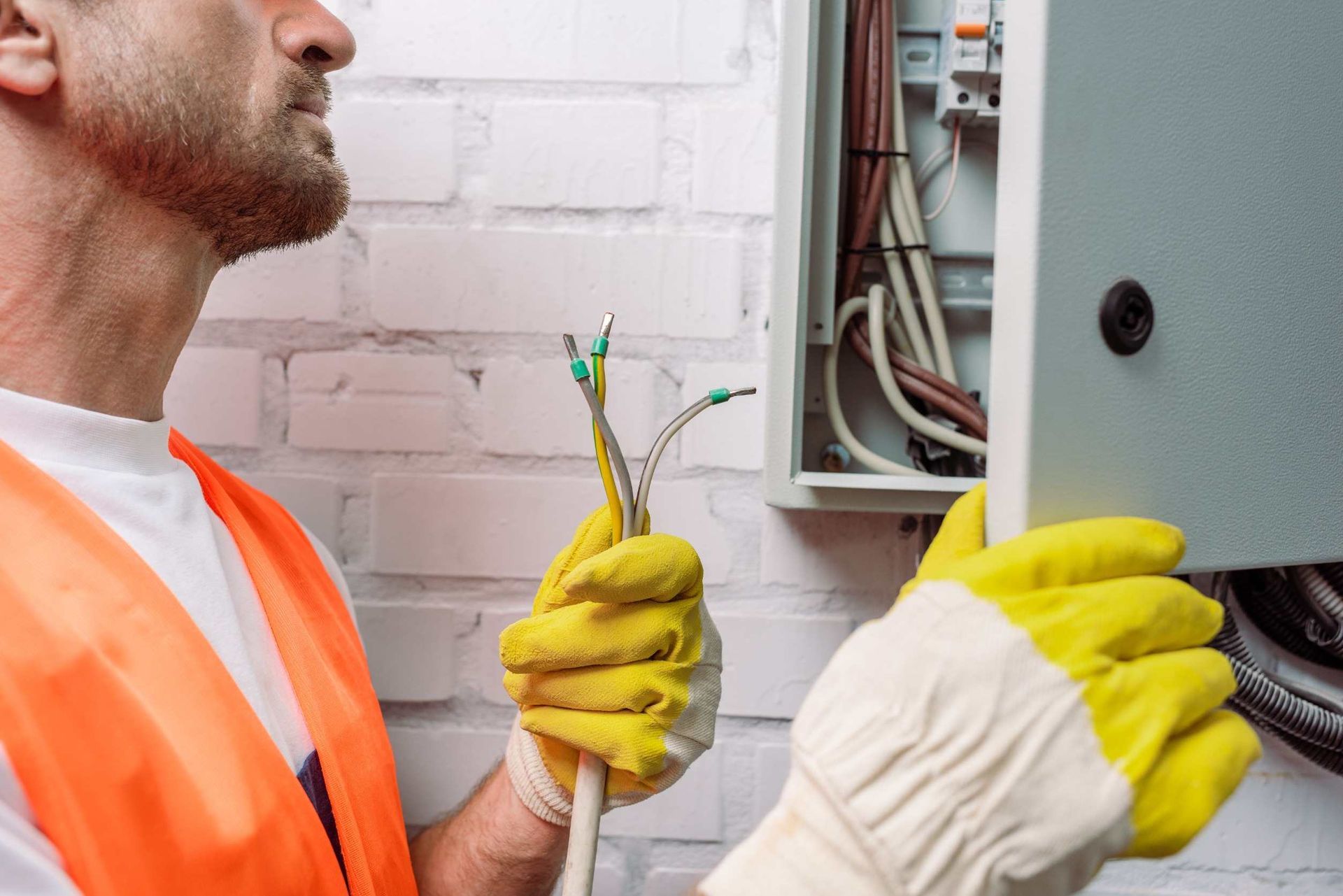 Un hombre que lleva guantes amarillos está trabajando en una caja eléctrica.