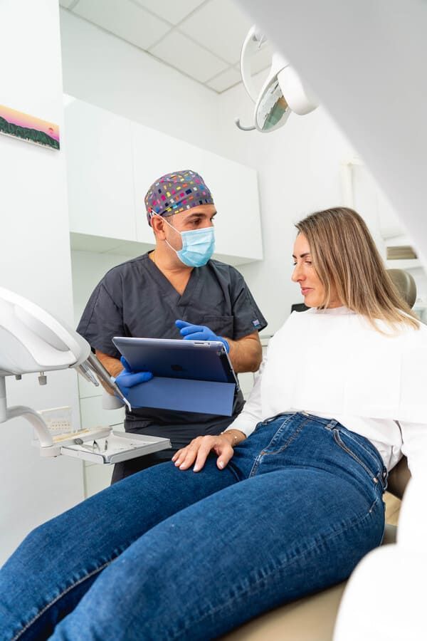 Una mujer está sentada en una silla dental hablando con un dentista.