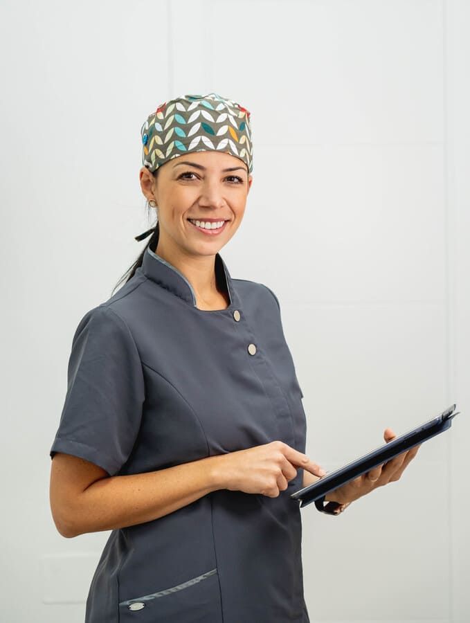 Una mujer con un traje de hospital sostiene una tableta y sonríe.