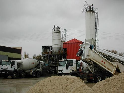 Una planta de hormigón con muchos camiones estacionados frente a ella.