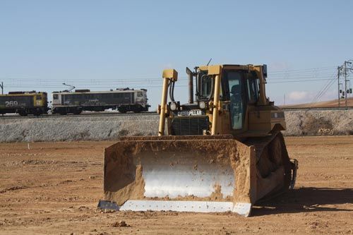 Una excavadora en un campo de tierra con un tren al fondo