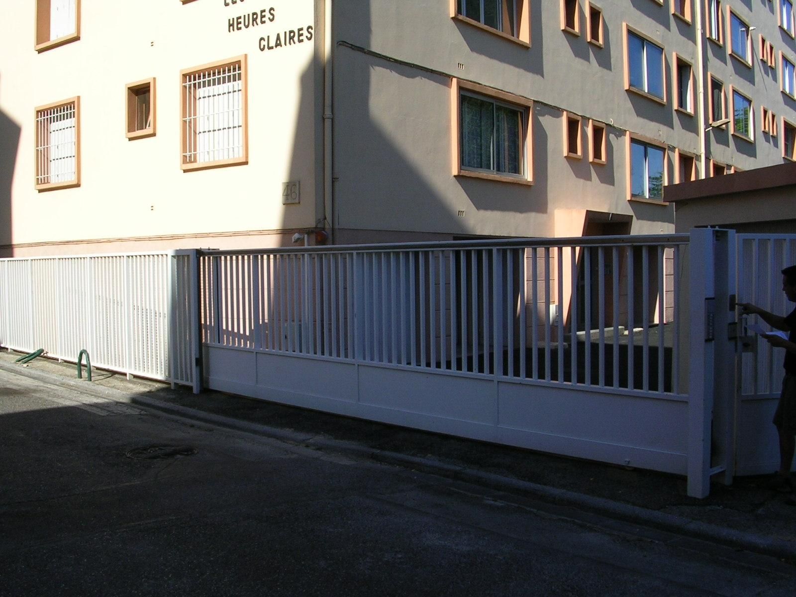 Grand portail coulissant ouvrant sur un parking résidentiel