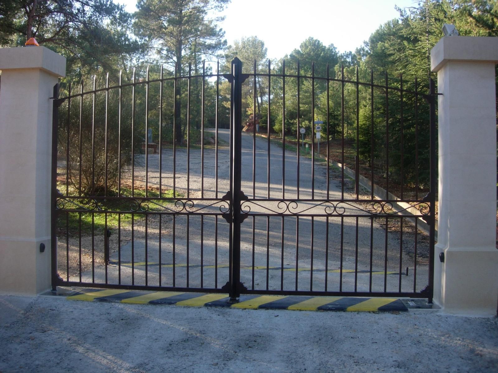 Portail noir qui donne sur une grande allée et un jardin