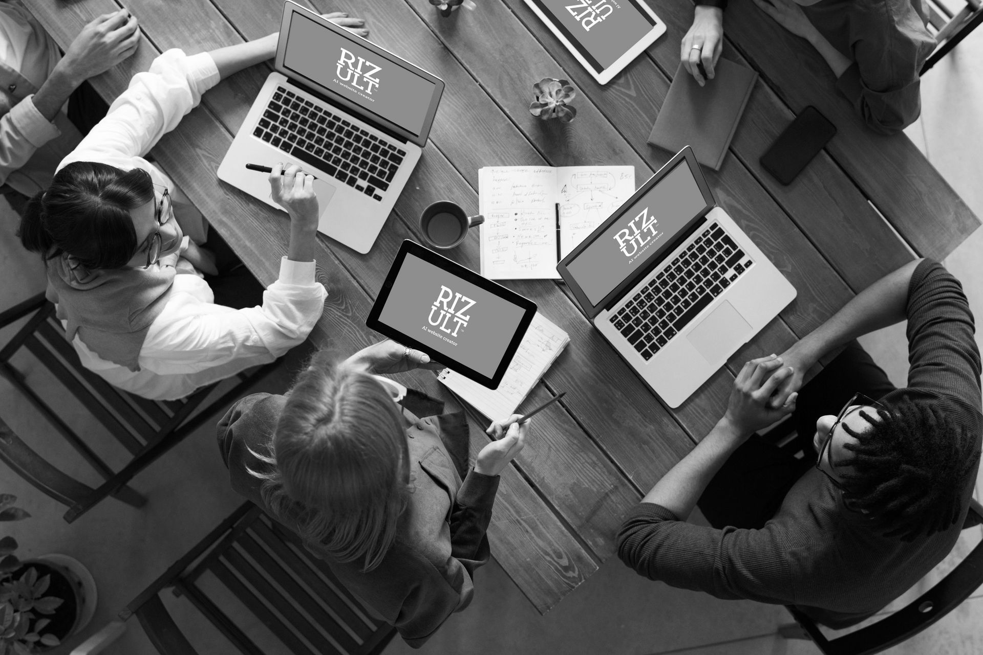 A group of people are sitting around a table with laptops and tablets.