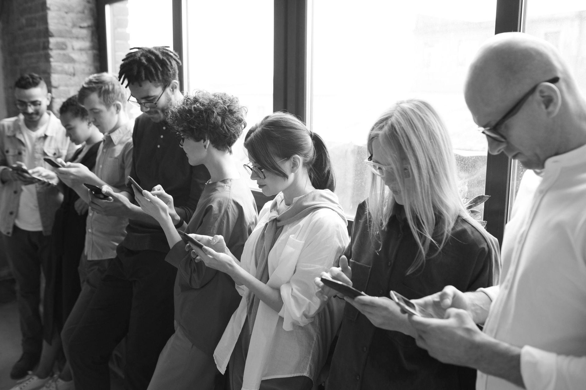 A group of people are standing in a line looking at their phones.