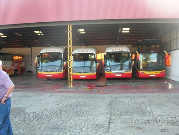 Una fila de autobuses rojos y amarillos están estacionados bajo un techo rojo.