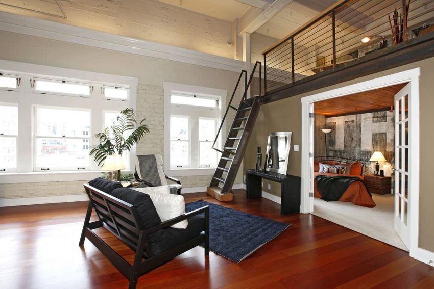 Salon loft moderne avec parquet, canapé noir, escalier et grandes fenêtres
