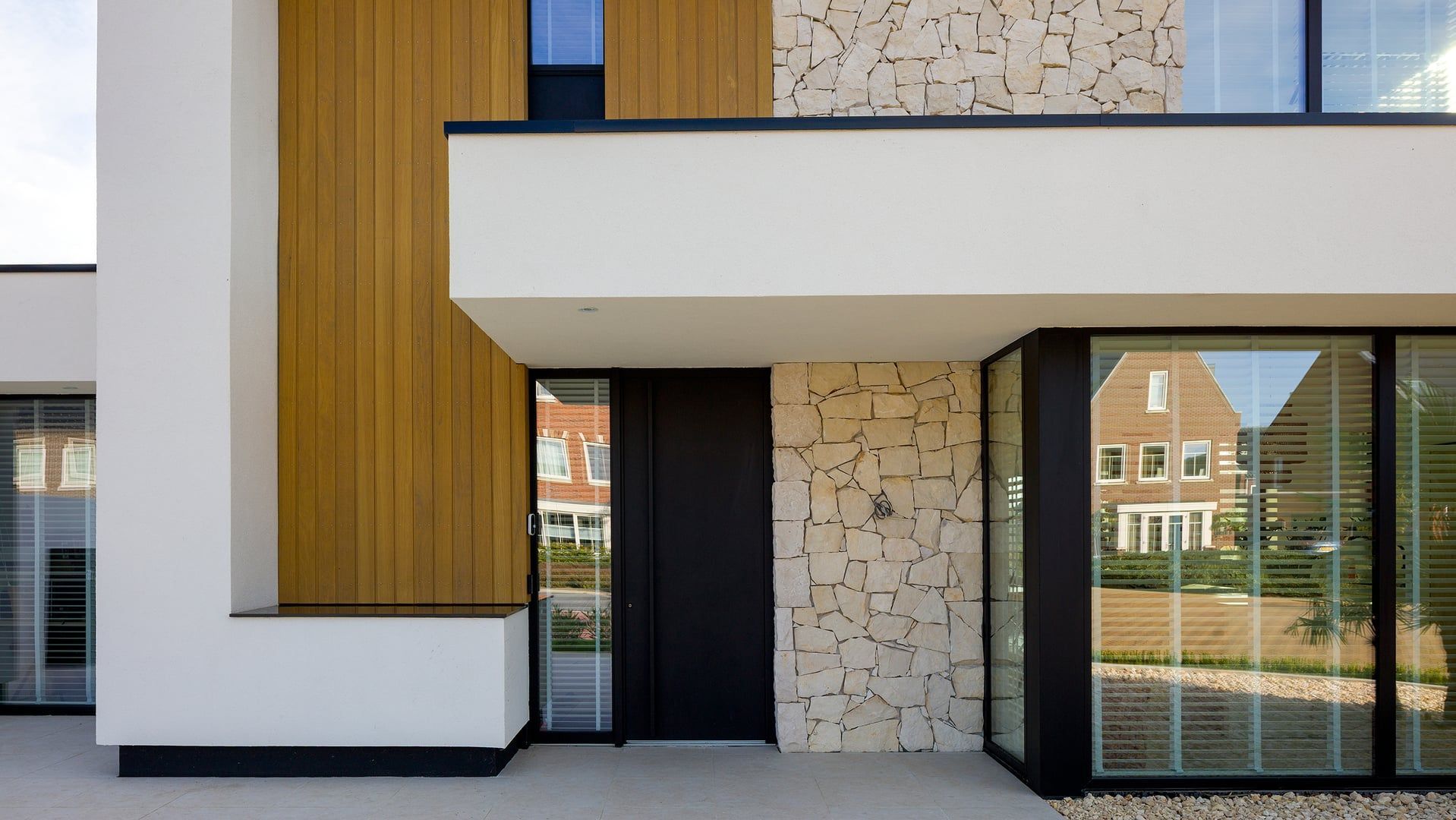 Entrée d'un immeuble moderne avec une façade blanche, en bois et en pierre et de grandes baies vitrées