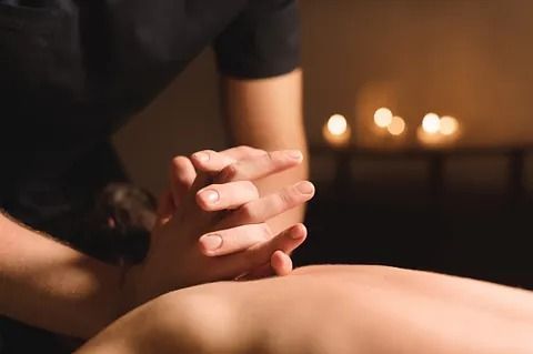 Una persona está recibiendo un masaje en una habitación oscura con velas de fondo.