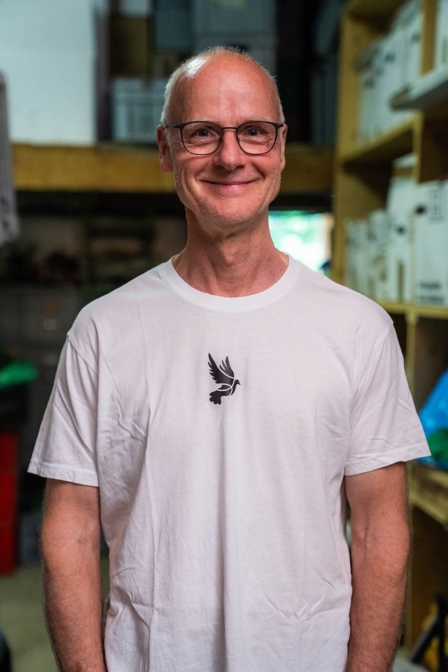 Mann mit Brille und weißem T-Shirt mit Vogelgrafik lächelt. Inneneinstellung.