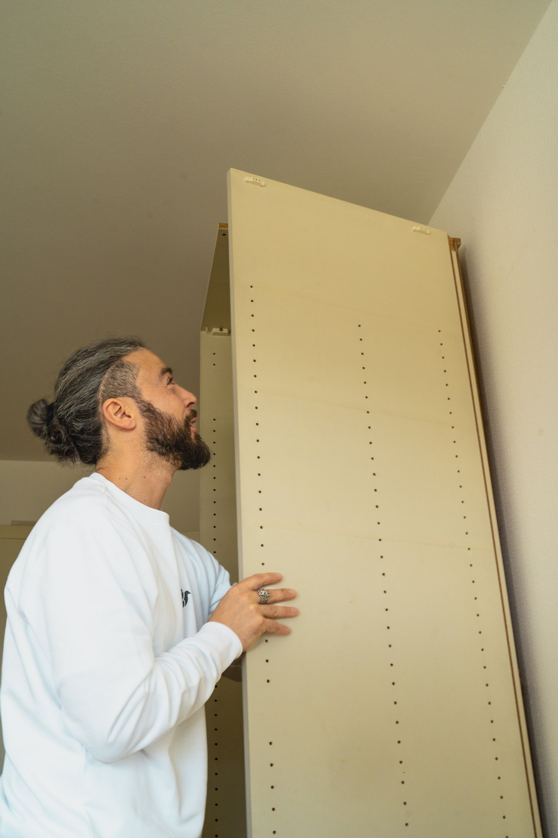 Mann installiert ein beiges Schrankregal an einer weißen Wand.