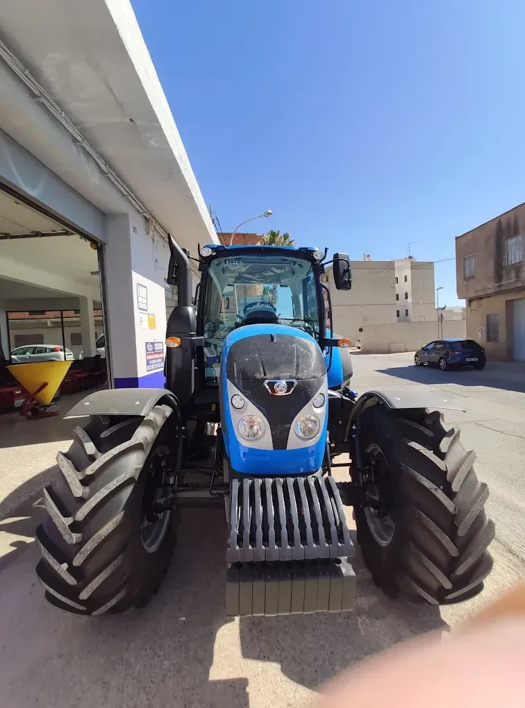 Tractor azul estacionado en la acera frente a un edificio en un día soleado.