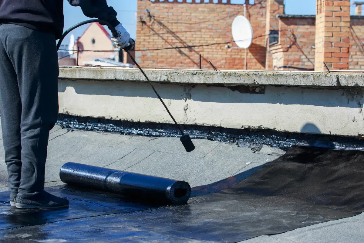 Persona aplicando una membrana para techos con un soplete sobre un tejado plano.
