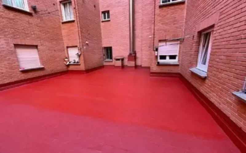 Patio revestido de rojo, rodeado de edificios de ladrillo con ventanas.