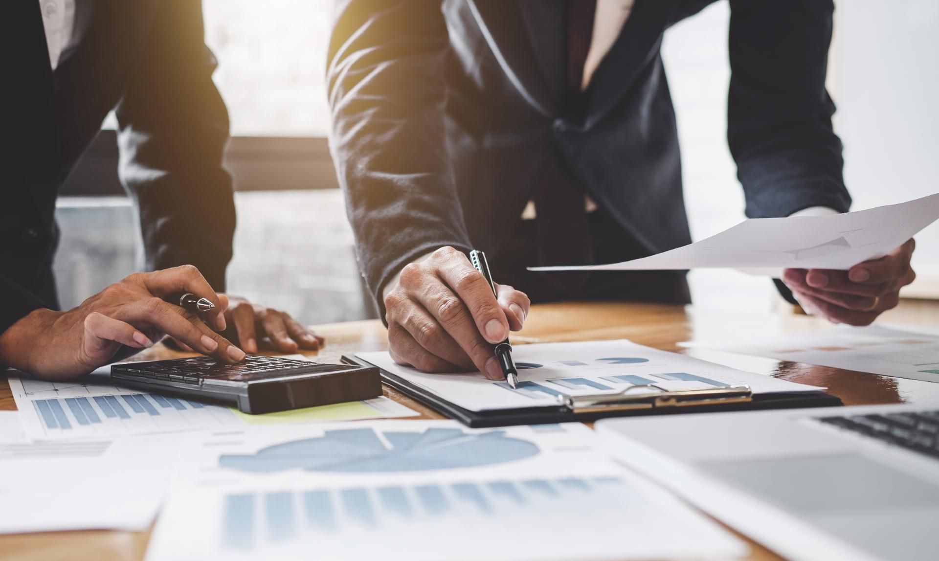 Zwei Steuerberater sitzen an einem Tisch und schauen auf Steuererklärungen und Dokumente.