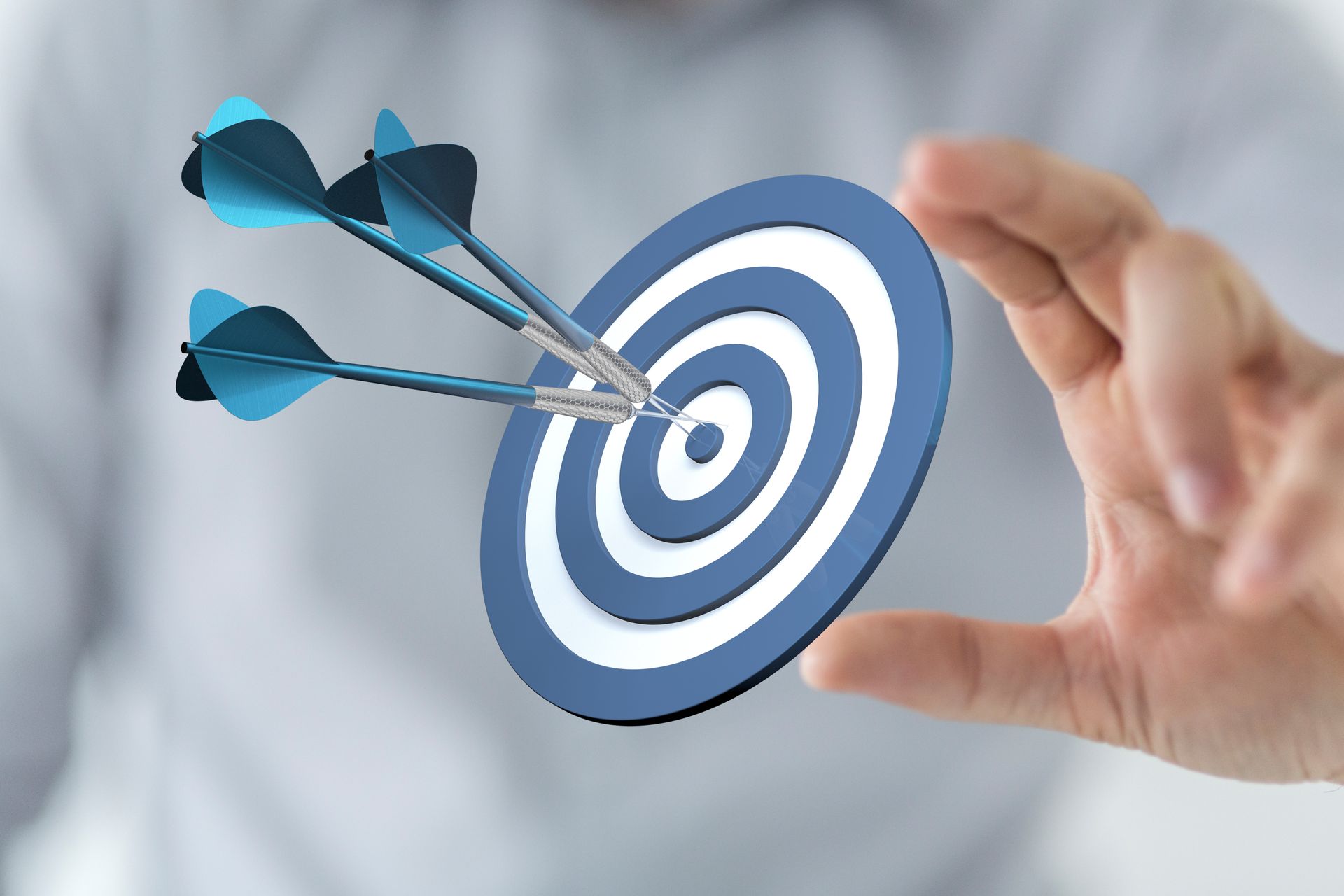 Main tenant une cible bleue et blanche avec trois fléchettes dans le mille.