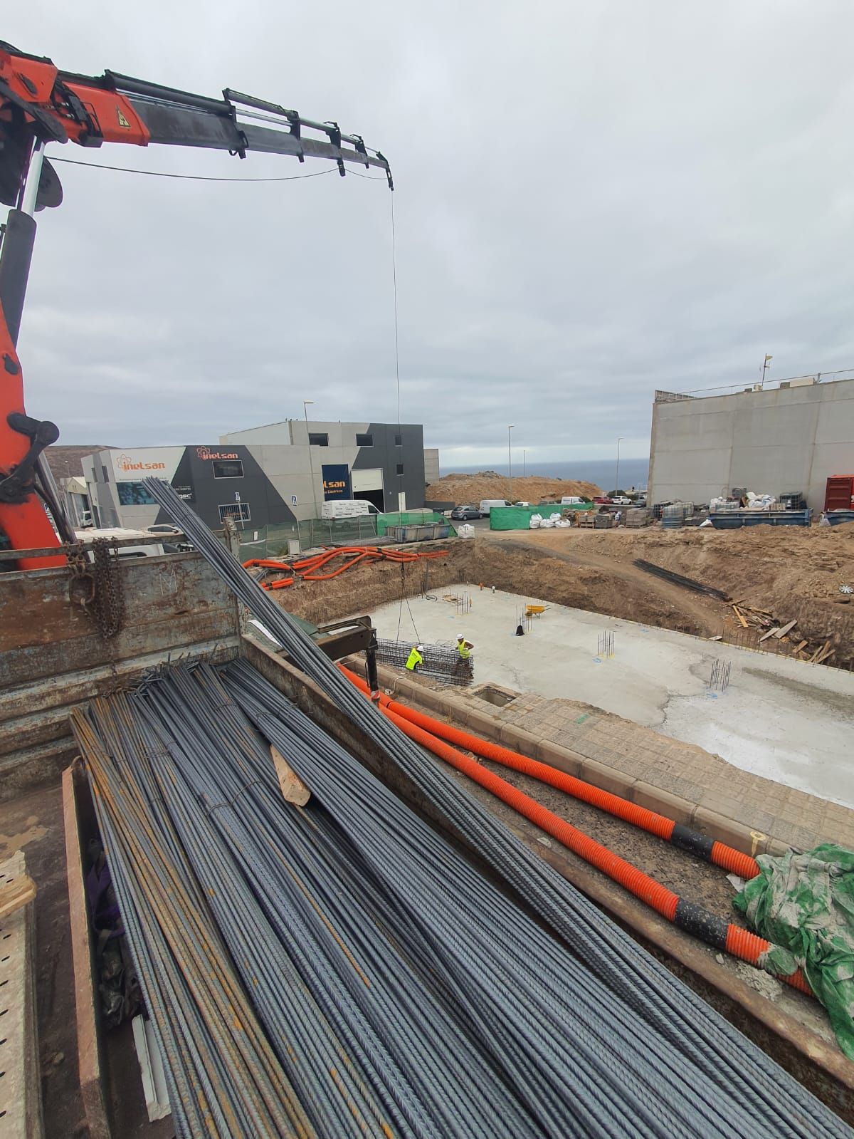 Una grúa está levantando una pila de barras de acero en un sitio de construcción.