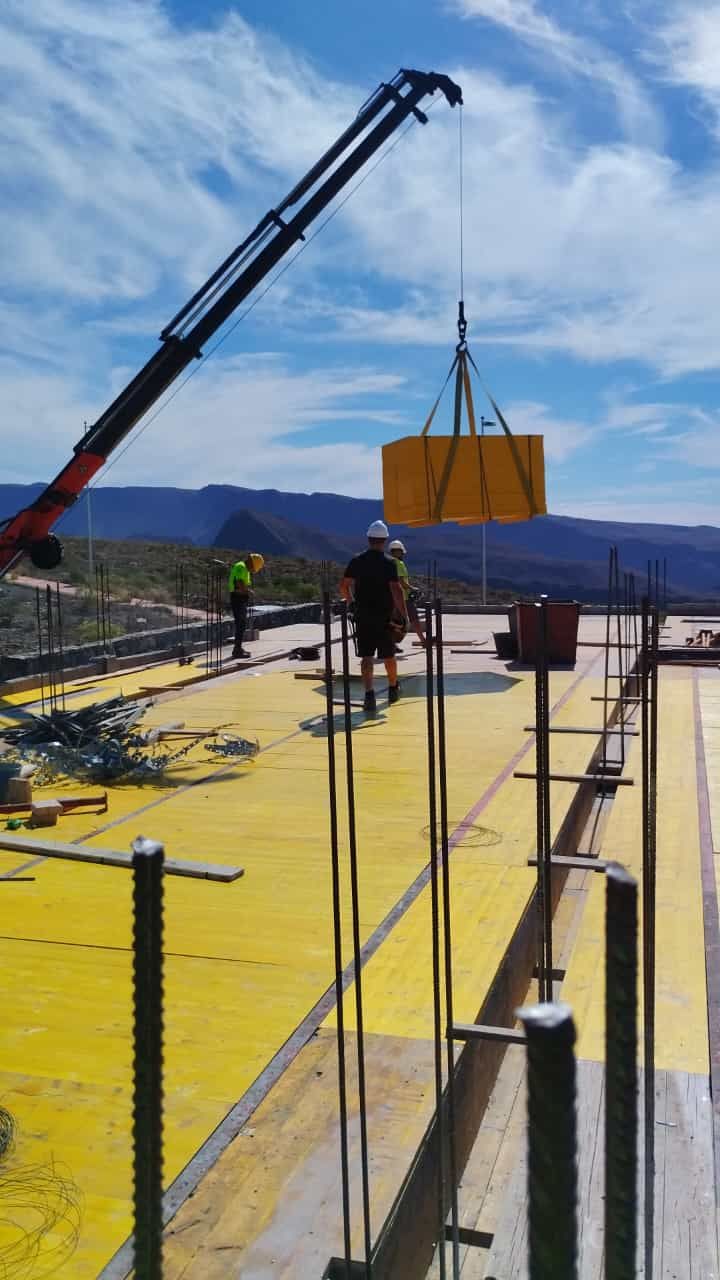 Una grúa está levantando una gran caja amarilla en un sitio de construcción.