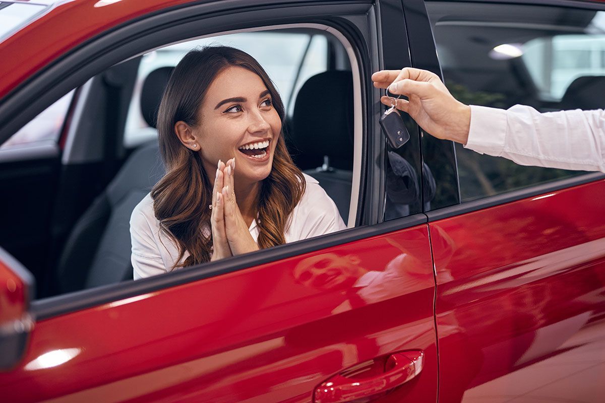 Femme souriante dans une voiture rouge qui reçoit les clefs de la part d'un vendeur