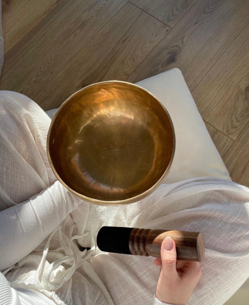 Une personne tient un bol en laiton avec un manche en bois.