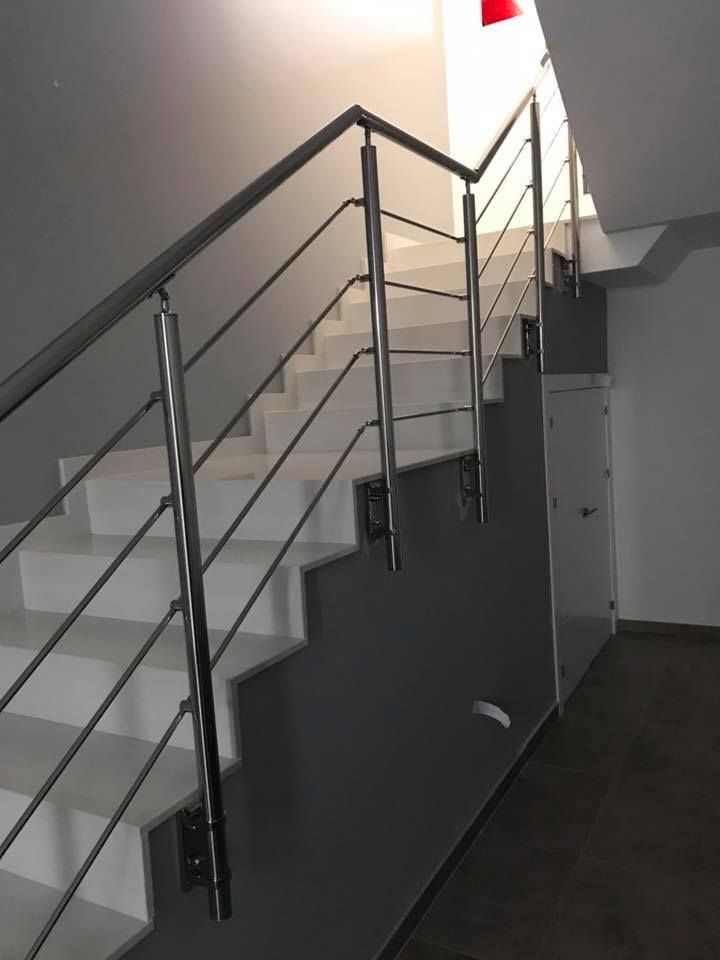 Escalera con escalones blancos, barandillas de acero inoxidable y pared gris.