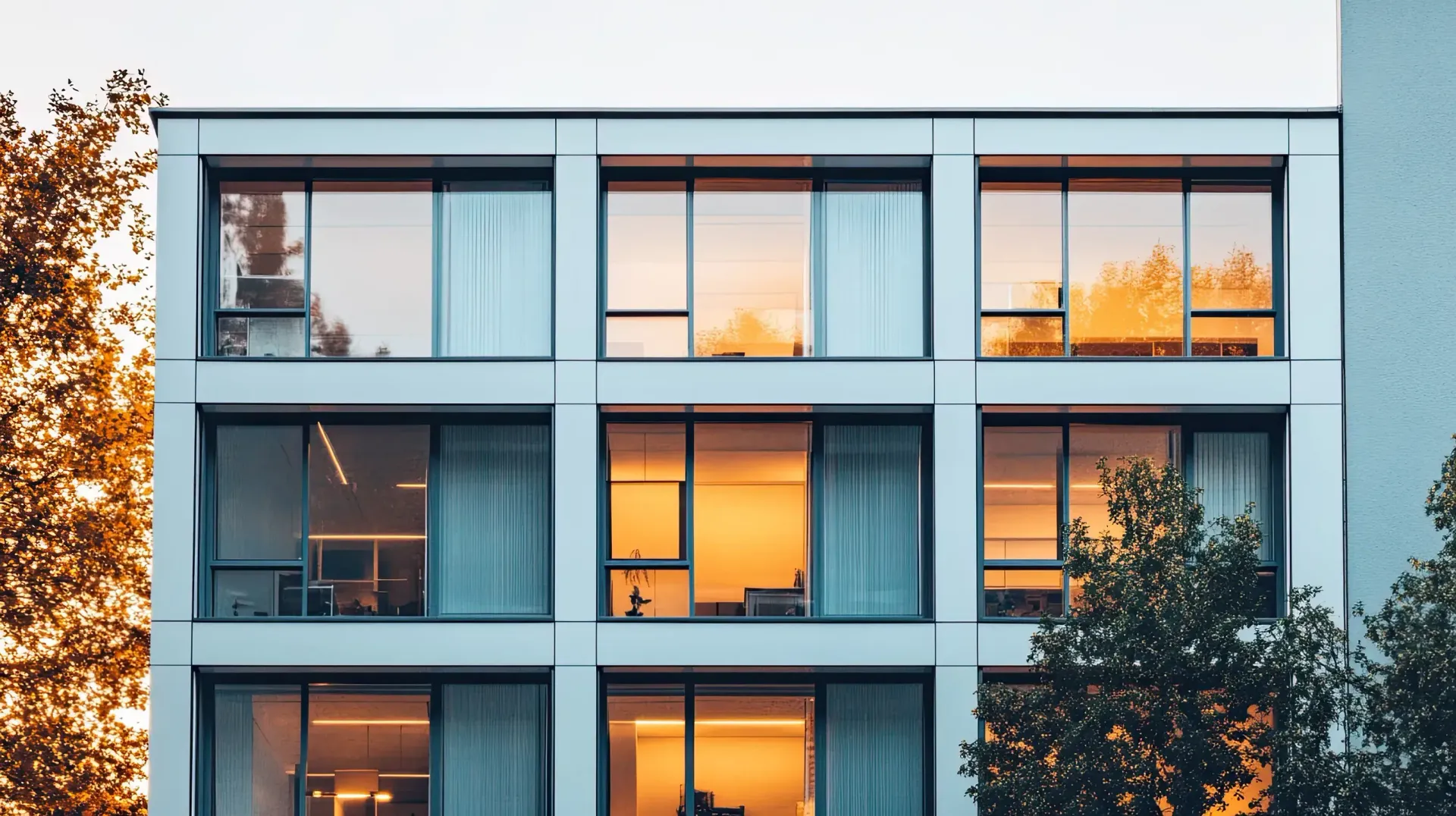 Fachada de edificio moderno con grandes ventanales que reflejan la cálida luz del sol.