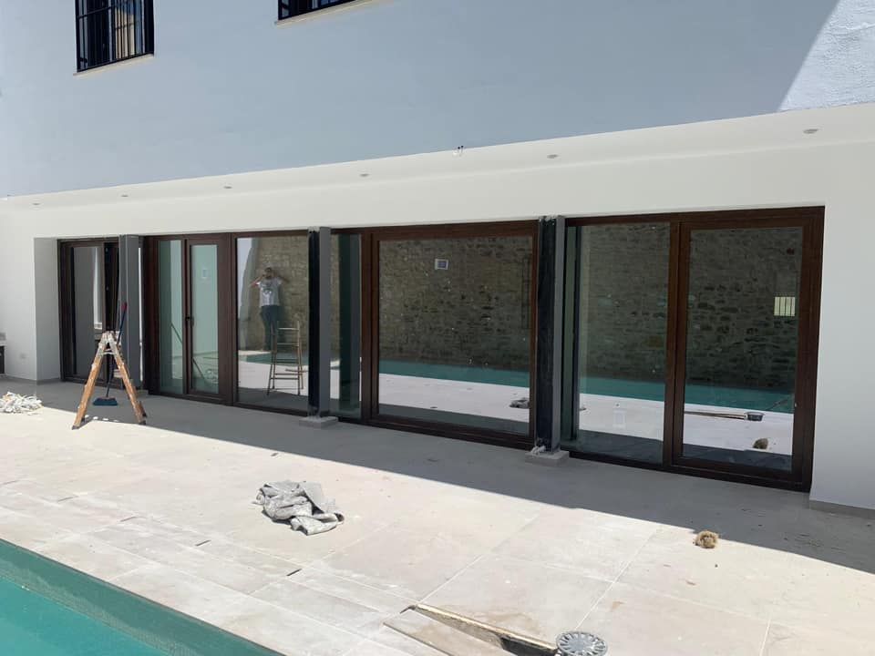 Un edificio blanco con puertas corredizas de vidrio con marco marrón que se abren a un patio y una piscina.