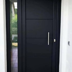 Puerta de entrada de color negro con paneles rectangulares y tirador vertical, con panel de cristal en el lateral.