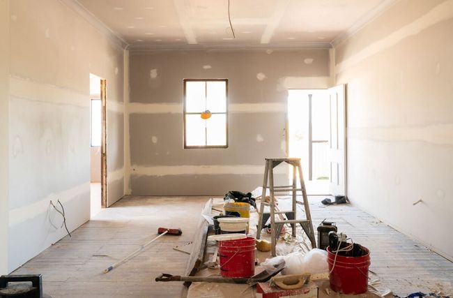 Una habitación en construcción con una escalera y cubos en el suelo.